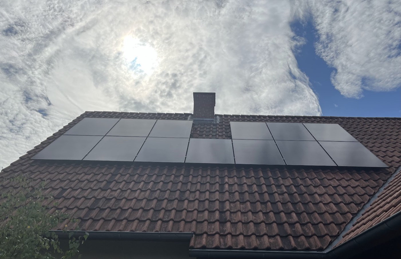 Photovoltaikmodule auf einem Ziegeldach mit Sonne und Wolken